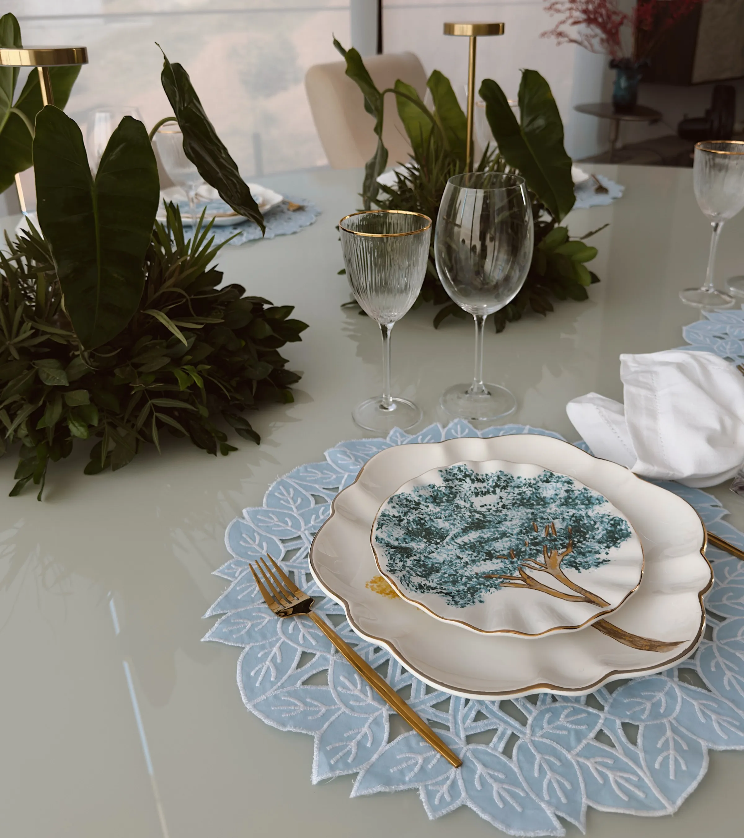 Mesa posta com louça artesanal, sousplat em linho azul e talheres dourados